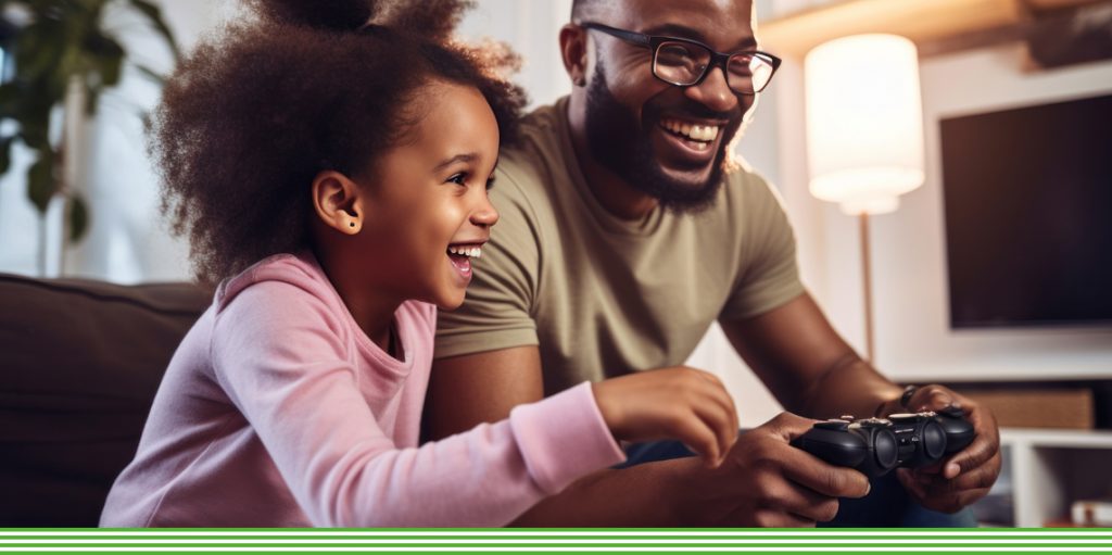 Father and daughter on sofa playing video game and laughing
