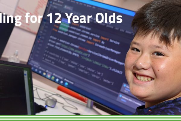 Chinese boy looking at camera and smiling with coding and computer screens in the background, in a lesson environment.